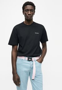 Μαύρο βαμβακερό μπλουζάκι με κοντά μανίκια και λευκό λογότυπο "Dickies". Συνδυασμένο με ανοιχτό μπλε τζιν και ροζ υφασμάτινη ζώνη με μαύρη αγκράφα.