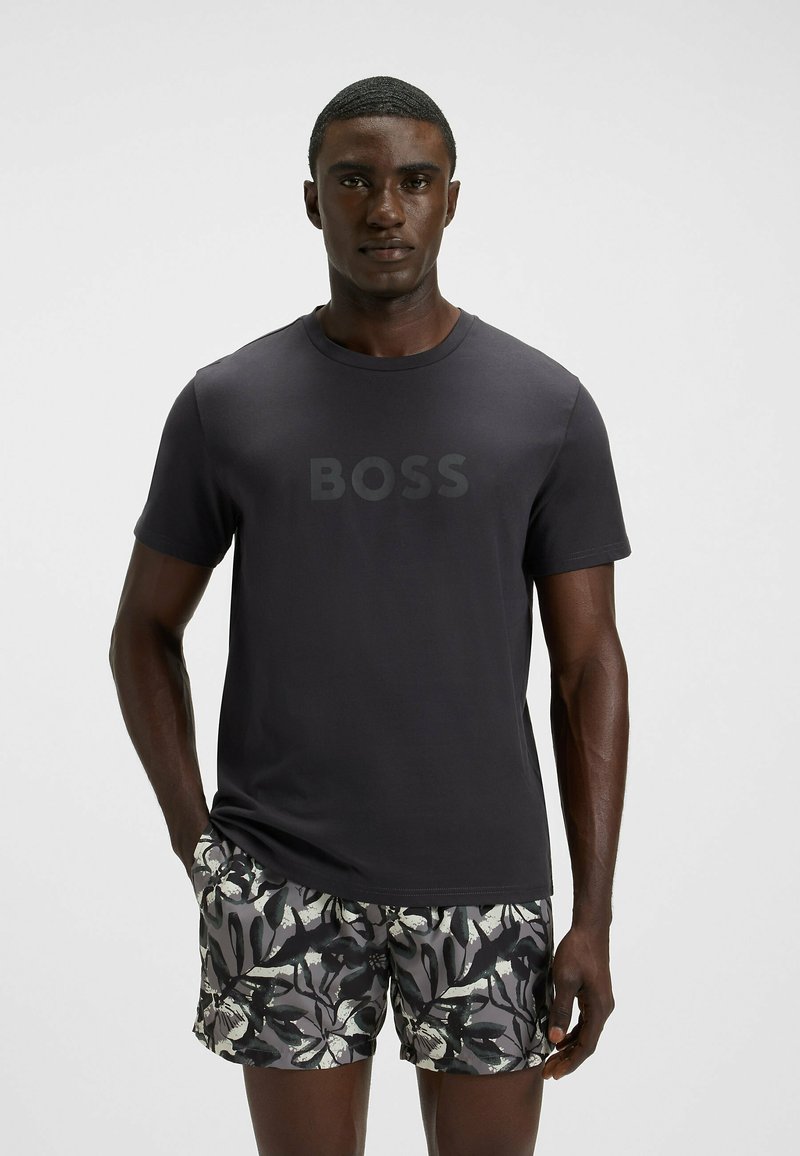 Mørk grå t-shirt med "BOSS" logo i en lidt lysere nuance, parret med mønstrede shorts med sort og hvidt løv.