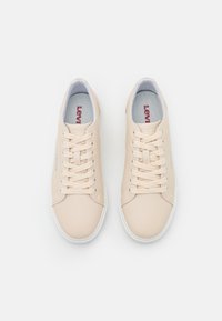 Baskets synthétiques beiges avec semelles en caoutchouc blanches, équipées de lacets, avec le logo Lev's sur le côté et une texture lisse.