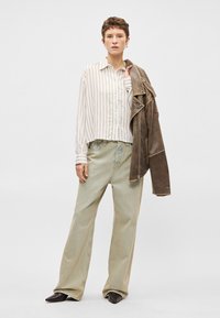 Svītraināta balta un beidzīga izgriezuma krekls, gaiši zaļi platās kājas džinsi, brūna ādas jaka pār plecu un melni šaurie kurpes.