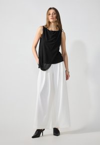 Black sleeveless top with draped fabric, paired with white wide-leg trousers and black heeled mules. Smooth texture and minimal design.