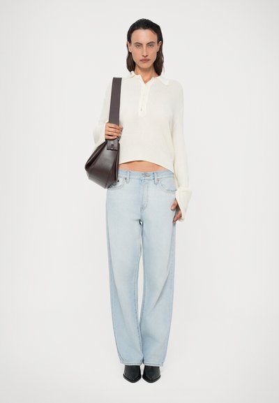 Svært tekstureret, cremefarvet sweater med krave og knapper, parret med lyseblå vidde ben jeans. Mørkebrun skuldertaske, sorte sko.