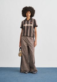 Black and brown striped short-sleeve top with "adidas" logo, paired with wide, leopard-print pants. Model holds a small bag.