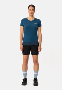 T-shirt de sport bleu à manches courtes avec un ourlet foncé, associé à un short noir et des chaussettes à rayures bleues. La chaussure présente un design robuste.