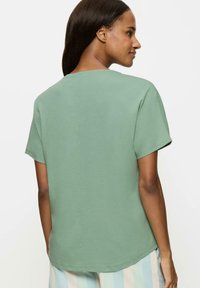 Koszulka z krótkim rękawem w stonowanej zieleni, wykonana z miękkiego materiału. Posiada okrągły dekolt i prosty krój z subtelnym przeszyciem z tyłu.