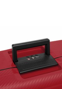 Valigia rossa con manico superiore nero, superficie testurizzata, lucchetto di sicurezza e porte USB. Finitura liscia con un sottile motivo in carbonio.