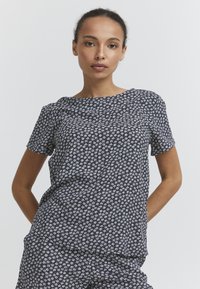T-shirt à manches courtes en tissu bleu foncé avec un motif floral blanc. Encolure ronde, coupe décontractée et texture douce, idéale pour un usage quotidien.