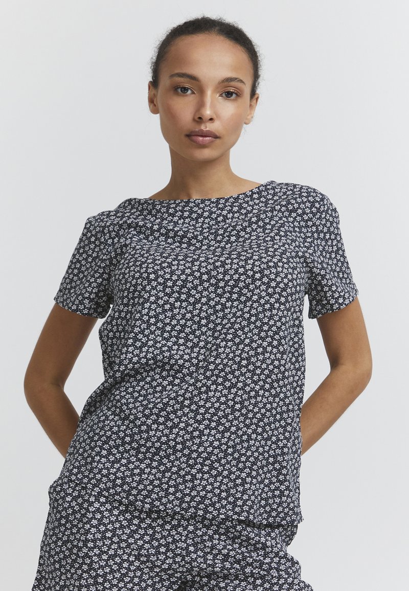 T-shirt à manches courtes en tissu bleu foncé avec un motif floral blanc. Encolure ronde, coupe décontractée et texture douce, idéale pour un usage quotidien.