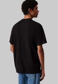 Czarna krótka koszulka z bawełny, o luźnym kroju, okrągłym dekolcie i schludnych szwach. Noszona z jasnoniebieskimi dżinsami.