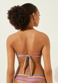 Bandeau-bikini med flerfärgade ränder, med knytning baktill och slät tyg. Designen betonar livfulla nyanser och minimalistisk stil.