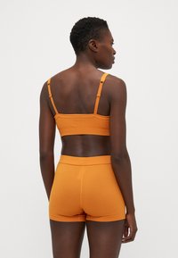 Ribbed oranžový bralet s nastaviteľnými ramienkami a zodpovedajúcimi šortkami. Má priliehavý strih s mäkkou textúrou a bezšvovou konštrukciou.