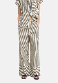 Set coordinato in cotone a righe, composto da una maglietta a maniche corte e pantaloni a gamba larga, nei colori crema e nero. Dettagli notevoli includono tasche laterali e rifiniture ai bordi.
