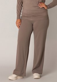 Bruine elastische taillebroek met een relaxte fit, voorzien van een gladde textuur en wijde pijpen, gecombineerd met witte sneakers.