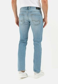Light blue denim jeans with a straight cut, back pockets, subtle stitching details, and a black brand label on the waistband.
