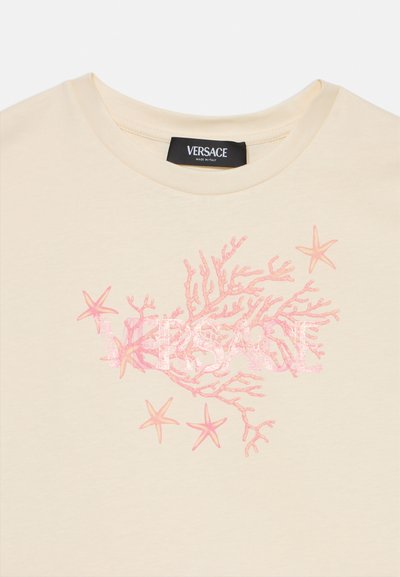Camiseta de algodón crema con un diseño de coral rosa y estrella de mar, con un logo "Versace" visible en un acabado brillante. Cuello redondo.