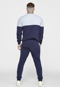 Tuta blu navy con sezione superiore grigio chiaro. Presenta una vestibilità comoda, polsini a coste e tasche posteriori. Realizzato in tessuto morbido e elasticizzato.