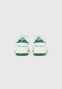 Λευκά και πράσινα αθλητικά παπούτσια Champion, εμφανιζόμενα από πίσω, με λεπτομέρειες λογότυπου και ανοιχτό μπεζ σόλες, σε απλό λευκό φόντο.