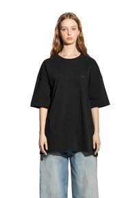 Czarny, oversize bawełniany t-shirt z okrągłym dekoltem i krótkimi rękawami, z subtelnym logo na piersi. Nosi się go z jasnoniebieskimi dżinsami.