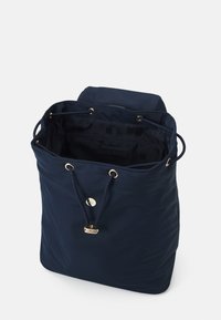 Mörkblå dragsko ryggsäck med guldöglor och knapp, visar öppen inredning med mönstrad svart foder och innerv pocket.