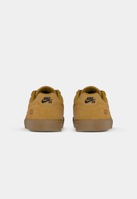 Buty Nike SB w odcieniu tanowego zamszu, z brązowymi podeszwami gumowymi. Posiadają klasyczne logo i numer 58 z tyłu. Zaokrąglony kształt i wyściełany kołnierz.