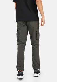 Spodnie cargo w ciemnooliwkowym kolorze, wykonane z lekkiego materiału, z dwiema bocznymi kieszeniami i elastycznymi mankietami, w połączeniu z czarnymi sneakersami.