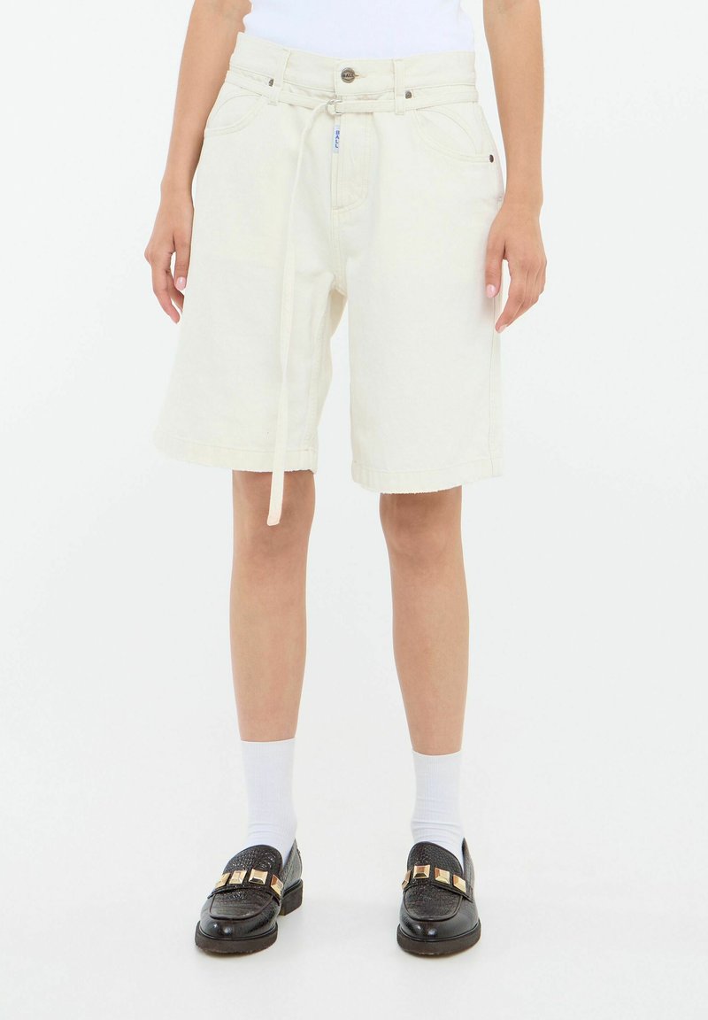 Pantalones cortos de mezclilla blanca de cintura alta, con cordones, bolsillos delanteros y un corte recto, combinados con mocasines negros y calcetines blancos.