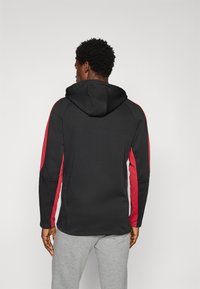 Mustahooded sweatshirt musta punarvoilla, joka on sileä pinta. Suunnittelussa on vetoketjullinen huppu ja istuvat hihansuut.