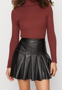 Burgundy rippad polotröja kombinerad med en svart plisserad läderskjol. Har en figursydd design och en slät, glänsande yta.