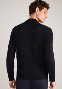 Schwarzer Strickpullover mit Rundhalsausschnitt und gerippten Bündchen. Glatte Textur, figurbetontes Design, von hinten betrachtet, ohne sichtbare Muster.