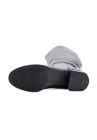 Bota gris hasta la rodilla con un upper suave y arrugado y una suela de goma negra resistente que presenta un agarre texturizado para tracción.