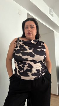 Top cu model negru și crem, cu un design drapat, având un triunghi pe umăr și un material texturat. Asortat cu pantaloni negri.