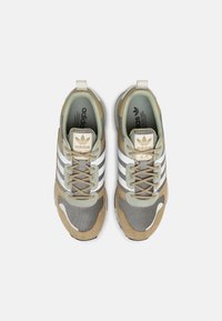 Adidas-sneakers med en grå mesh-ovandel och tan mocka detaljer, tre vita ränder och en beige tummelapp.