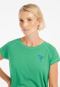 Grön atletisk t-shirt, kortärmad, rundad nederdel, blå "PROTEST"-logotyp och palmträdsmotiv på bröstet, slät textur, lätt material.