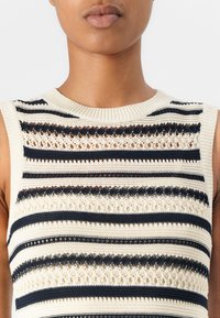 Débardeur en tricot sans manches avec des rayures crème et marine alternées, des motifs de dentelle complexes, et un col et un ourlet côtelés.