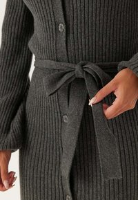 Cardigan grigio a coste con bottoni frontali e cintura legata in vita. Presenta una texture verticale e maniche lunghe, offrendo una silhouette aderente.