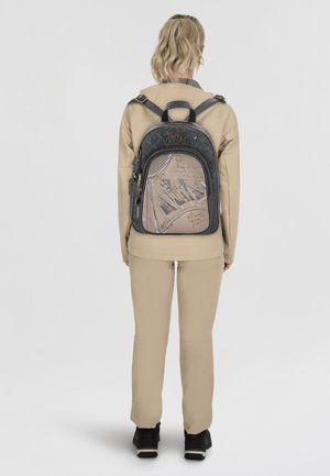 Dunkelblauer Rucksack mit strukturierter Oberfläche, ausgestattet mit einem hellbraunen Frontpanel, das mit Skizzen und Schriftzügen verziert ist. Mit Reißverschlussfächern und einem Logo-Highlight.