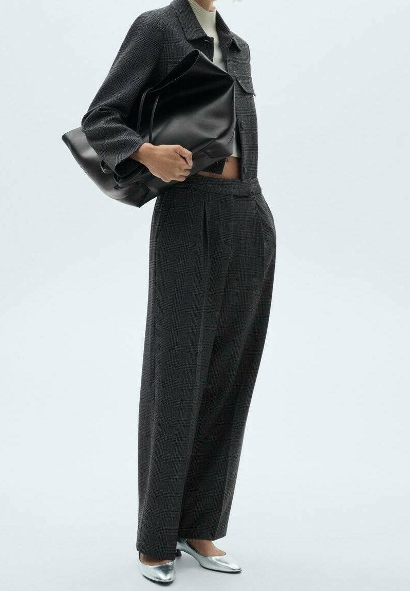 Czarna kraciasta kurtka w połączeniu z wysokim stanem szarych spodni, srebrnymi butami z ostrym noskiem oraz czarną skórzaną torbą na ramię.