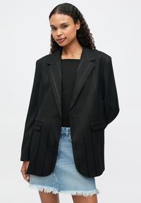 Mustmustriibuline must bleiser ühe nupu kinnitusega, küljetaskudega ja laia kraega, koos helesinise teksaseelikuga.