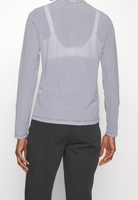 Långärmad skjorta i ljusgrå med ett strukturerat mönster. Har en rund halsringning och en lös passform. Kombinerad med mörka byxor.