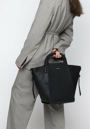 Schwarze Leder-Tote-Tasche mit strukturiertem Design, abgerundeten Handgriffen und goldenen Hardware-Details. Die Tasche hat eine weiche Textur und ein seitliches Etikett.