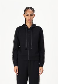 Sudadera negra con cremallera y bolsillo frontal, con acentos texturizados en las mangas y cordones. Hecha de una tela suave con un acabado liso.
