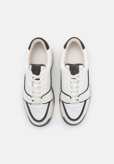 White leather sneakers with black accents, textured gray rubber sole, round toe, and lace-up front. Features a distinct layered design.