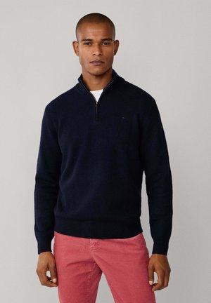 Marineblauwe gebreide trui met een ritskraag, geribde manchetten en zoom. Gekocht over een wit shirt, gecombineerd met lichtroze broeken.