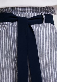 Pruhovaná látka v modré a bílé barvě s pevným námořnickým opaskem uvázaným do mašle. Textura vypadá lehce a prodyšně.