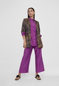 Purple button-up shirt, oversized animal print blazer in navy and tan, wide-leg purple pants, and black sandals with a bow detail.