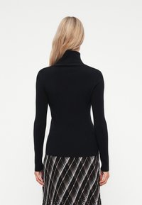 Jersey de cuello alto negro con mangas largas, diseño ajustado, textura suave, llevado sobre una falda estampada con líneas diagonales en negro y colores claros.