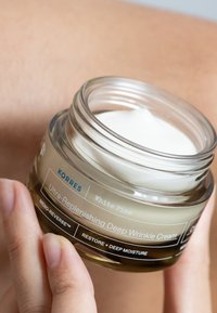 Korres Ultra-Replenishing Deep Wrinkle Cream i en klar glasburk med ett vitt lock. Etiketten inkluderar "White Pine" och andra produktdetaljer.