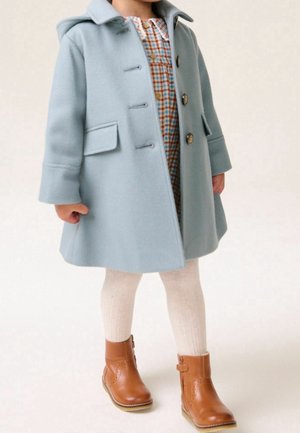 Barn iført en lyseblå hættejakke over en ternet kjole, cremefarvede strømpebukser og brune læderankelstøvler på en ensfarvet baggrund.