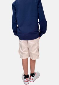 Felpa navy, pantaloni cargo beige chiaro e sneaker bianche con dettagli rossi e logo "HUGO". Mostra un look casual e sportivo.