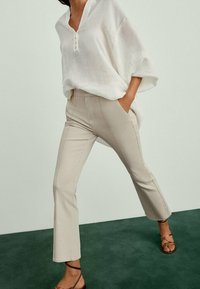 Chemisier en lin blanc surdimensionné avec un col en V et des boutons, associé à un pantalon beige ajusté avec des coutures latérales, porté avec des sandales à brides marron.